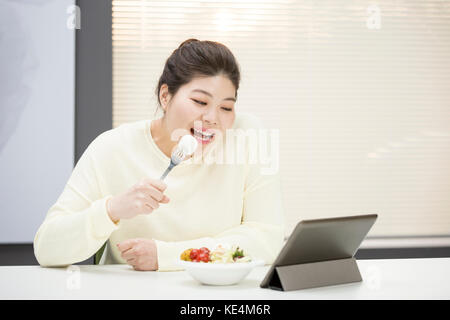 Portrait der junge lächelnde fette Frau essen Verkauf mit einem elektrischen Tablet Stockfoto