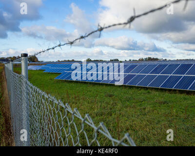 Solaranlage oder Photovoltaik Farm hinter Metall Zaun auf der grünen Wiese mit dramatischen bewölkter Himmel im Norden Deutschlands. Stockfoto