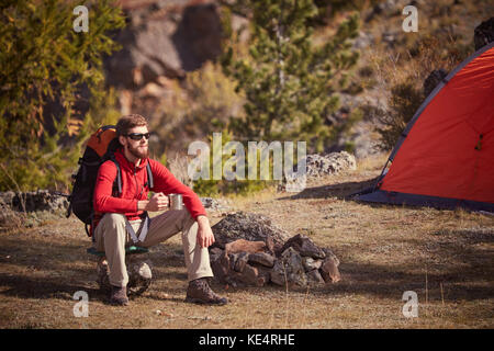 Backpacker in Ruhe in der Nähe von orange Zelt mit Becher in der Hand. Stockfoto