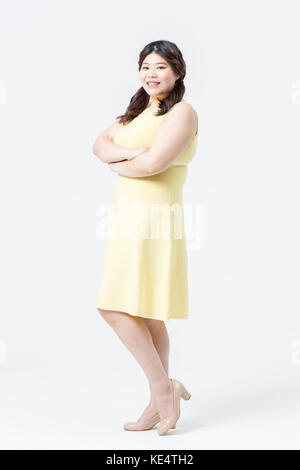 Seitenansicht der junge lächelnde fette Frau im gelben Kleid posiert Stockfoto