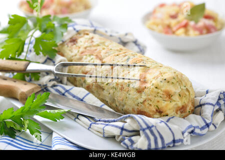 Uncut bayerische Semmelknödel in einem aufgerollten Geschirrtuch gekocht, Sauerkraut mit Speck im Hintergrund Stockfoto