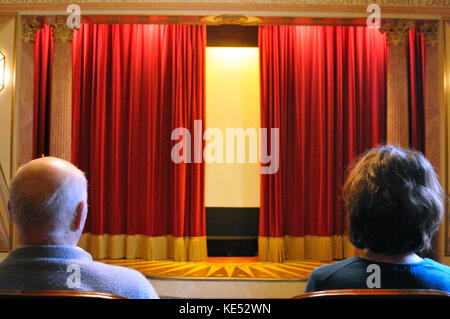 Velvet rote Vorhänge leicht öffnen, zeigt der Mann und die Frau, die in ein eigenes Kino der 1920er Jahre, Anfang der 30er Jahre Stil. Hell erleuchtet. Stockfoto