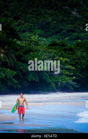 Auf unberührten Strand in Rio de Janeiro, Surfer, die seine Board, das zeigt eine brasilianische Flagge Stockfoto