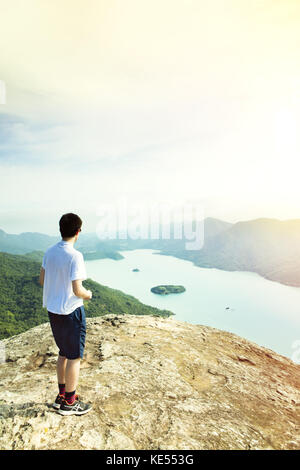 Junger männlicher Wanderer, der auf der grünen Küste in der Nähe von Paraty, Brasilien, auf dem Saco de Mamangua von Sugar Loaf Peak aus blickt Stockfoto