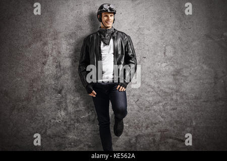 Biker lehnte sich gegen eine rostige graue Wand, und wenn man die Kamera Stockfoto