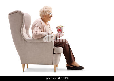 Reife Frau mit einer Portion Popcorn und 3D-Brille in einem Sessel sitzt auf weißem Hintergrund Stockfoto