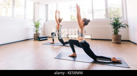 Zwei junge Menschen arbeiten im Innenbereich. Klasse Yoga. Der Mann und die Frau nach vorne Strecken im Krieger darstellen. Stockfoto