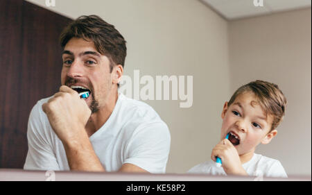 Vater und Sohn Zähneputzen im Badezimmer. Junger Mann mit seinem Sohn zusammen Zähneputzen und Suchen im Spiegel. Stockfoto