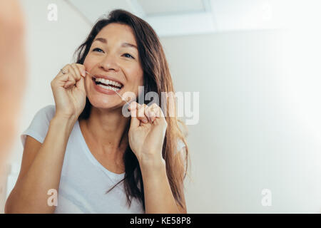 Frau Suchen im Badezimmerspiegel und die Verwendung von Zahnseide Zähne zu reinigen. Reflexion der Frau im Badezimmer Spiegel beim Zähneputzen am Morgen Stockfoto