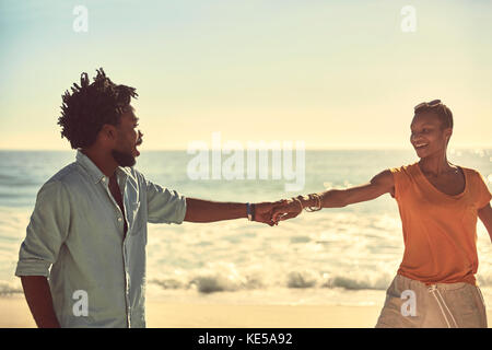 Liebevolles junges Paar, das Hände am sonnigen Sommerstrand hält Stockfoto