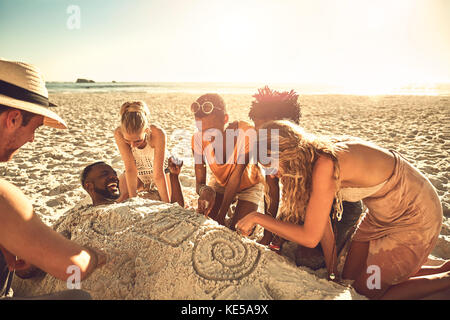 Junge Freunde begraben und zeichnen Freund in Sand auf sonnig Sommerstrand Stockfoto