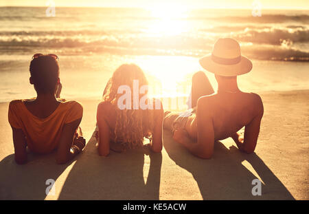 Unbeschwerte junge Freunde, die sich am sonnigen Sommersonnenuntergang am Meeresstrand entspannen Stockfoto
