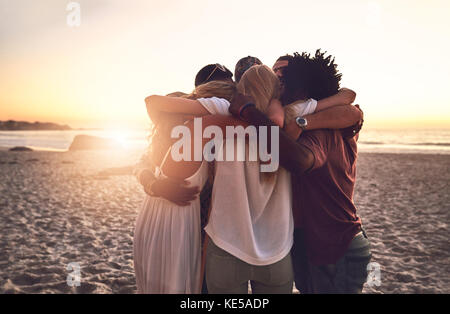 Junge Freunde umarmen sich in einem huddle am Sonnenuntergang Sommer Strand Stockfoto