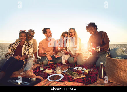 Porträtieren Sie junge Freunde, die am sonnigen Sommerstrand ein Picknick genießen Stockfoto
