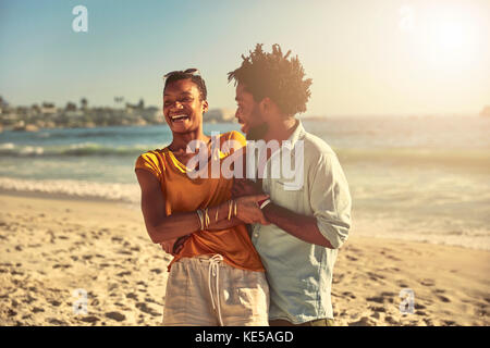 Verspielte junge Paar umarmt und lachend auf sonnigen Sommer Ozean Strand Stockfoto