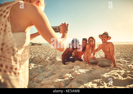 Junge Frau mit Kamera-Handy fotografieren Freunde im sonnigen Sommer Strand Stockfoto