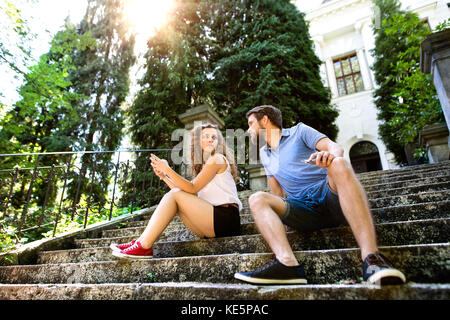 Schöne junge Paar mit smart phone sitzen auf der Treppe in der alten Stadt, beobachten oder etwas zu lesen. sonnigen Frühlingstag. Stockfoto