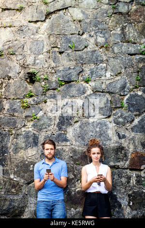 Wunderschönes junges Paar mit Smartphones, die in der Altstadt an einer Steinmauer stehen und etwas sehen oder lesen. Sonniger Frühlingstag. Stockfoto