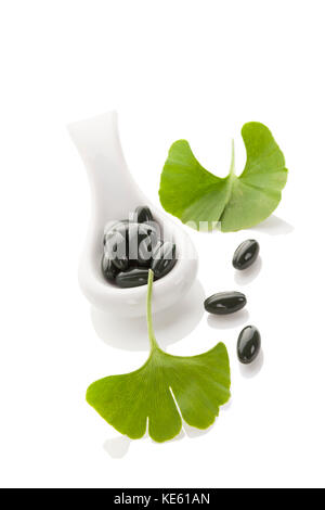 Ginkgo Blätter mit Gel Kapseln auf weißem Hintergrund mit Reflexion isoliert. alternative Medizin, Nahrungsergänzung, natürliche Heilmittel. Stockfoto