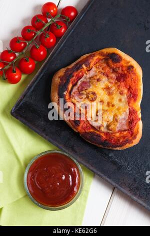 Top down Sicht auf hausgemachte Pizza, unvollständig geformt und mit Ketchup und Kirschtomaten getan Stockfoto