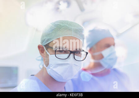 Portrait zuversichtlich männlichen Chirurgen trägt Brillen und chirurgische Maske in Operationssaal Stockfoto