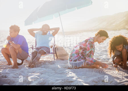 Multi-ethnische Familie entspannen und spielen im Sand im sonnigen Sommer Strand