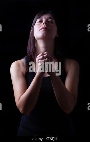 Treue Frau beten, Hände in der Anbetung gefaltet mit Kopf auf und geschlossenen Augen in religiösem Eifer für Gott, auf einem schwarzen Hintergrund. Gebet Gläubigen beten Stockfoto