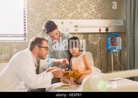 Männlich Arzt mit Otoskop auf Teddybär von Mädchen Patienten Im Krankenhauszimmer Stockfoto