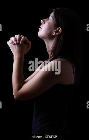 Treue Frau beten in Anbetung zu Gott suchen, in der Hoffnung, mit Hände gefaltet und religiöse Inbrunst auf einem schwarzen Hintergrund. beten Gebet hoffnungsvoll Falten Stockfoto