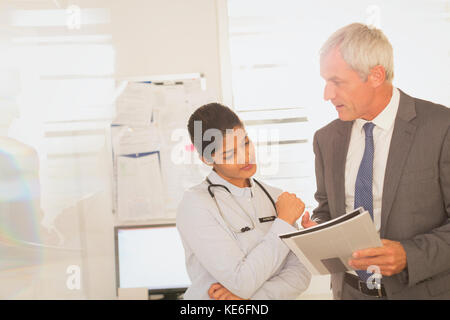 Weibliche Ärztin und männliche Krankenhausverwalterin überprüfen Papierkram Stockfoto