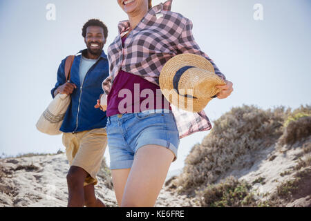Lächelndes, enthusiastisches Paar, das auf einem sonnigen Sommersandstrandweg spazierengeht Stockfoto