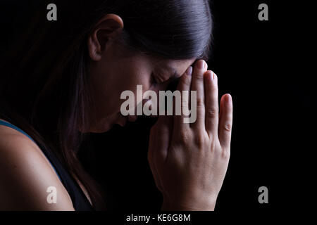 Treue Frau zu beten, die Hände gefaltet in der Anbetung mit Kopf nach unten zu Gott und Augen in religiöser Inbrunst geschlossen, auf einem schwarzen Hintergrund/Gebet portrait Stockfoto