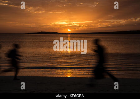 Silhouette Jogger laufen am Strand mit goldenen Sonnenuntergang über dem Meer im Hintergrund Stockfoto