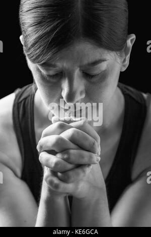 Low Key Porträt einer gläubigen Frau zu beten, die Hände gefaltet in Gottesdienst, Kopf und Augen in religiöser Inbrunst geschlossen, auf einem schwarzen Hintergrund. Stockfoto