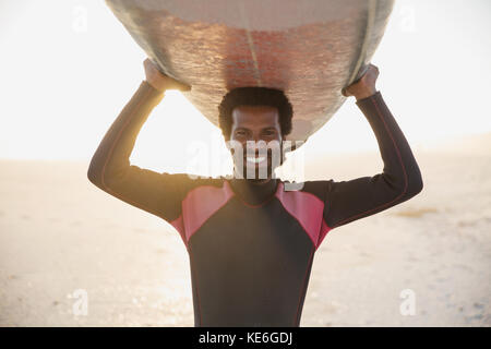 Portrait lächelnder, selbstbewusster Surfer mit Surfbrett über dem sonnigen Sommerstrand Stockfoto