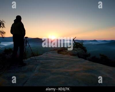Silhouette der Landschaft Fotograf auf Spitze oben misty Valley. bunte Sonne heben über neblige Landschaft. Stockfoto