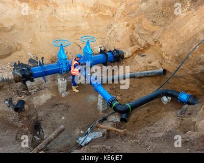 Technische Experten offene Tor Ventil auf 500 mm Wasser trinken Rohre verbunden mit neuen schwarzen gemeinsame Mitglieder in alte Pipeline System. Mann control Fini Stockfoto