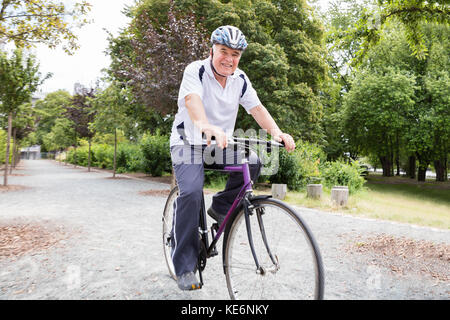 Lächelnd älterer Mann Reiten Fahrrad im Park Stockfoto