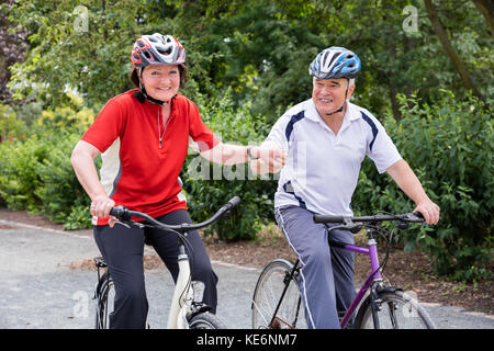 Lächelnd Senior Paar Hände halten beim Reiten Fahrrad im Park Stockfoto
