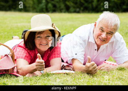 Senior Paar liegt in einem Park mit Daumen hoch Stockfoto