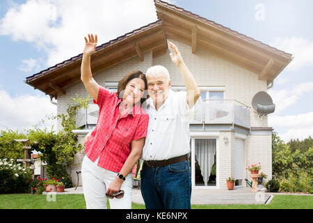 Gerne älteres Paar heben Ihre Arme vor dem Haus Stockfoto