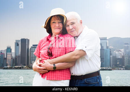 Portrait Of Happy Senior Paar umarmen Vor Hong Kong Skyline der Stadt. Stockfoto