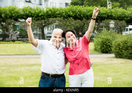 Portrait von Elder Senior Paar heben Ihre Arme in Park Stockfoto