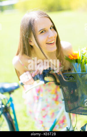 Porträt der jungen schönen Frau mit langem Haar im Sommer Park. Neben einem Fahrrad mit einem Korb mit Blumen Stockfoto
