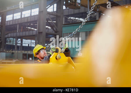 Arbeiter in der Fabrik, der die Kette an die Ausrüstung angehängt hat Stockfoto