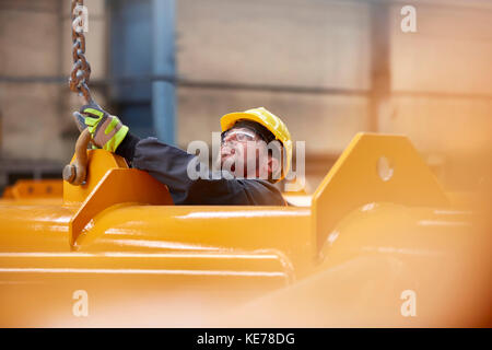 Männlicher Arbeiter, der die Kette an die Ausrüstung im Werk anfügt Stockfoto