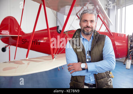 Porträt Lächeln, selbstbewusste männliche Flugzeug Pilot bei Biplanaren im Hangar Stockfoto