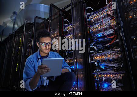 Fokussierter männlicher IT-Techniker mit digitalem Tablet im Dunkeln des Servers Zimmer Stockfoto