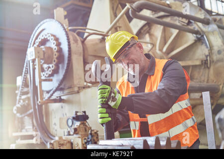 Männlicher Arbeiter mit großem Schraubenschlüssel auf Maschinen in der Fabrik Stockfoto