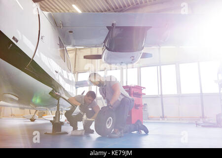 Männliche Mechanik zur Festsetzung der Räder auf dem Flugzeug im Hangar Stockfoto